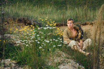 young medieval hunter rests on the slope of a hill covered with flowers and herbs
