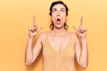 Young beautiful hispanic woman wearing casual clothes amazed and surprised looking up and pointing with fingers and raised arms.