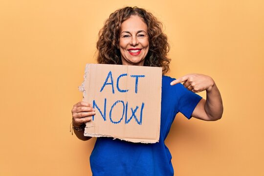 Middle age beautiful woman asking for react holding banner with act now message smiling happy pointing with hand and finger