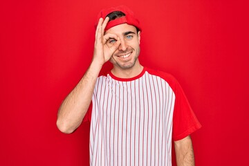 Fototapeta premium Young handsome sporty man with blue eyes wearing striped baseball t-shirt and cap doing ok gesture with hand smiling, eye looking through fingers with happy face.