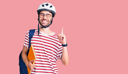 Young hispanic man wearing student backpack and bike helmet holding binder surprised with an idea or question pointing finger with happy face, number one