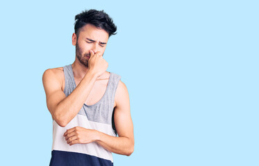 Young hispanic man wearing casual clothes smelling something stinky and disgusting, intolerable...