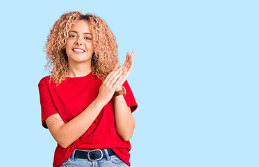Young blonde woman with curly hair wearing casual red tshirt clapping and applauding happy and joyful, smiling proud hands together