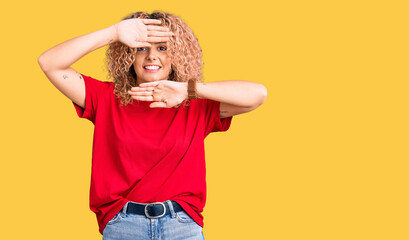 Young blonde woman with curly hair wearing casual red tshirt smiling cheerful playing peek a boo...