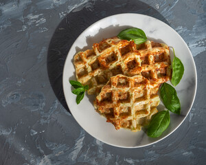 Spicy zucchini waffles with added cheese, decorated with basil leaves on a gray plate on a dark...