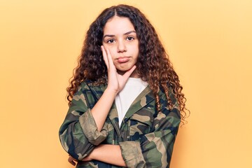 Beautiful kid girl with curly hair wearing camouflage jacket thinking looking tired and bored with depression problems with crossed arms.