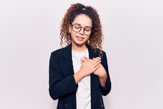 Beautiful kid girl with curly hair wearing business clothes and glasses smiling with hands on chest with closed eyes and grateful gesture on face. health concept.