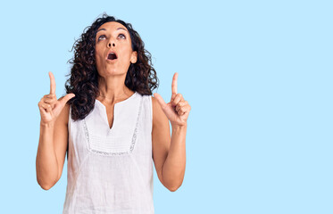 Middle age beautiful woman wearing casual sleeveless t shirt amazed and surprised looking up and...