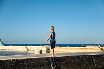 Young boy standing on concrete wall at the beach near Newcastle Baths, NSW Australia