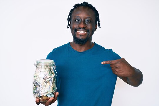 Young african american man with braids holding jar with savings pointing finger to one self smiling happy and proud