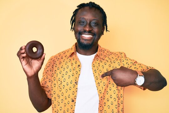 Young african american man with braids holding donut pointing finger to one self smiling happy and proud