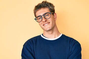 Young handsome man wearing casual clothes and glasses happy face smiling with crossed arms looking...