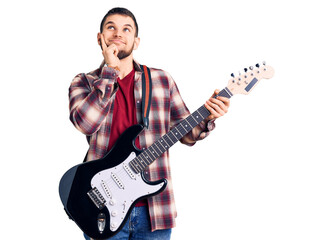 Young handsome man playing electric guitar serious face thinking about question with hand on chin,...