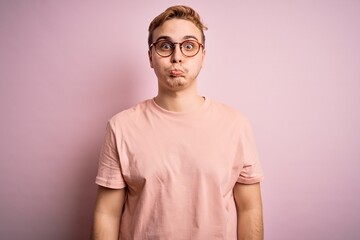 Young handsome redhead man wearing casual t-shirt standing over isolated pink background puffing cheeks with funny face. Mouth inflated with air, crazy expression.