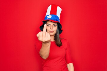 Young beautiful brunette woman wearing united states hat celebrating independence day Showing middle finger, impolite and rude fuck off expression