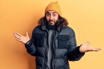 Young arab man wearing casual winter clothes clueless and confused expression with arms and hands...