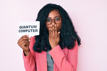 Beautiful african woman holding quantum computer banner covering mouth with hand, shocked and...