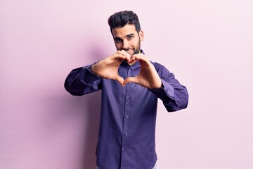 Young handsome man with beard wearing casual shirt smiling in love doing heart symbol shape with hands. romantic concept.