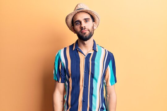 Young handsome man with beard wearing summer hat and shirt relaxed with serious expression on face. simple and natural looking at the camera.