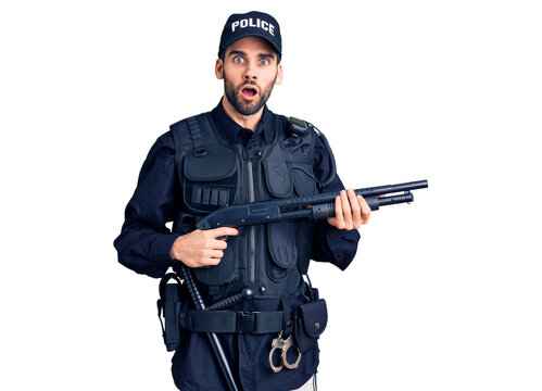 Young handsome man with beard wearing police uniform holding shotgun scared and amazed with open mouth for surprise, disbelief face