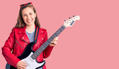 Fototapeta premium Young beautiful blonde woman playing electric guitar looking positive and happy standing and smiling with a confident smile showing teeth
