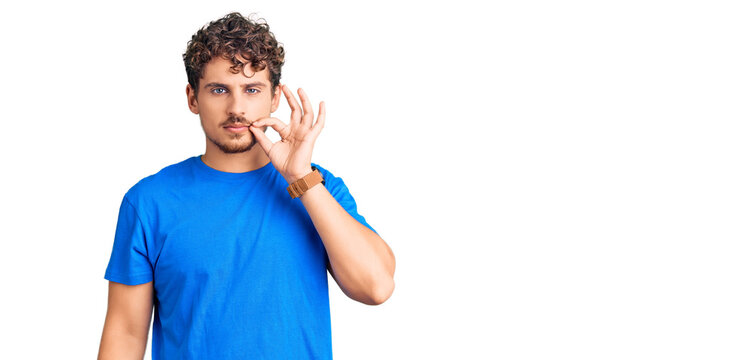 Young handsome man with curly hair wearing casual clothes mouth and lips shut as zip with fingers. secret and silent, taboo talking