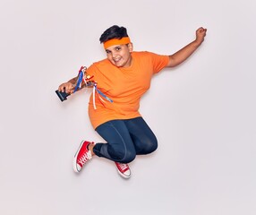 Adorable hispanic kid wearing sportswear smiling happy. Jumping with smile on face holding trophy over isolated white background