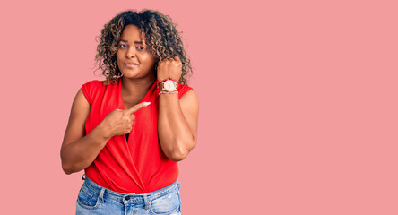 Young african american plus size woman wearing casual style with sleeveless shirt in hurry pointing...