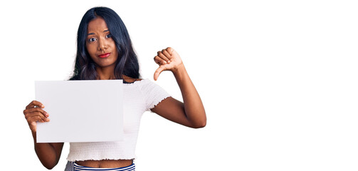 Young indian girl holding blank empty banner with angry face, negative sign showing dislike with...