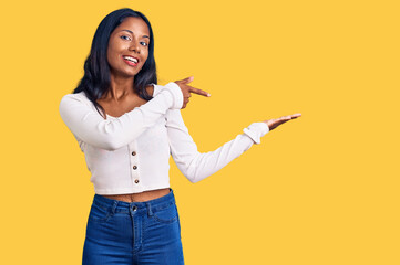 Young indian girl wearing casual clothes amazed and smiling to the camera while presenting with hand and pointing with finger.