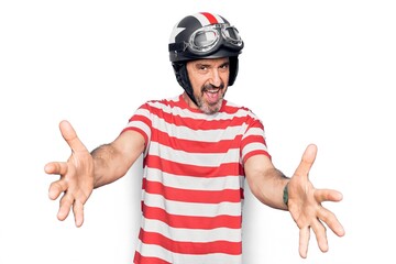 Middle age handsome motorcyclist man wearing moto helmet over isolated white background looking at the camera smiling with open arms for hug. Cheerful expression embracing happiness.