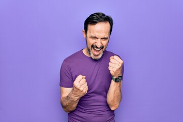 Middle age handsome man wearing casual purple t-shirt standing over isolated background celebrating surprised and amazed for success with arms raised and eyes closed