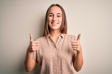 Young beautiful woman wearing casual shirt standing over isolated white background success sign doing positive gesture with hand, thumbs up smiling and happy. Cheerful expression and winner gesture.