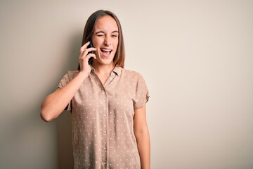 Young beautiful woman having conversation talking on the smartphone over white background winking...