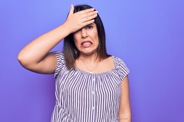 Fototapeta na wymiar Young beautiful brunette woman wearing casual striped t-shirt standing over purple background surprised with hand on head for mistake, remember error. Forgot, bad memory concept.