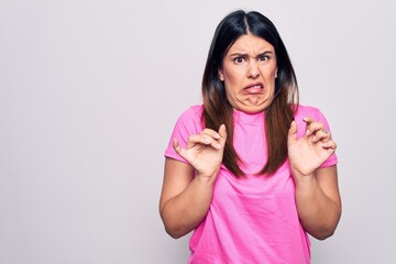 Young beautiful brunette woman wearing casual pink t-shirt standing over white background disgusted...