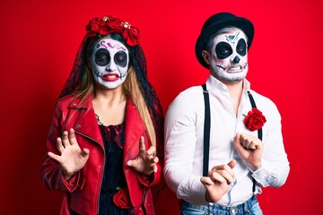 Couple wearing day of the dead costume over red disgusted expression, displeased and fearful doing...