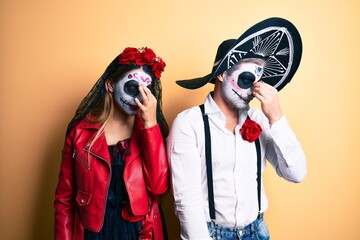 Couple wearing day of the dead costume over yellow tired rubbing nose and eyes feeling fatigue and headache. stress and frustration concept.