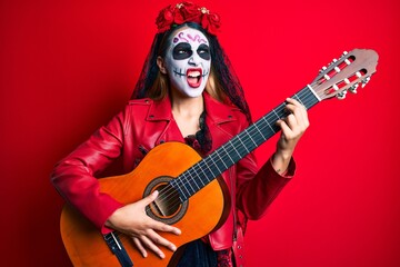 Woman wearing day of the dead costume playing classical guitar angry and mad screaming frustrated and furious, shouting with anger. rage and aggressive concept.