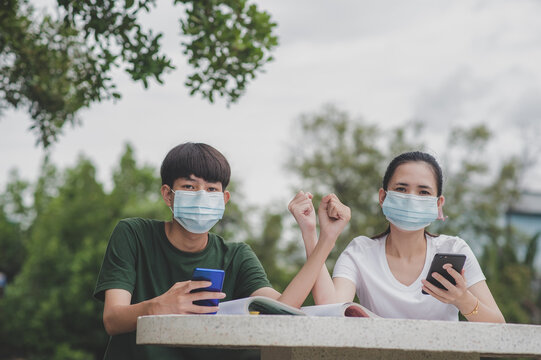Asian Boy and  Girl in face mask using mobile smartphone,Concept new normal social distancing - Powered by Adobe