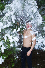 young man in a winter forest sprinkles snow to harden the body