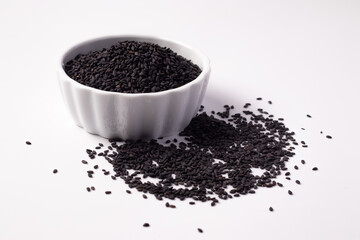 Black sesame seeds in a white ceramic cup on a white background