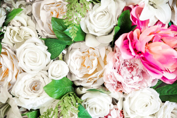 Artificial flowers background of white and pink roses and green leaves