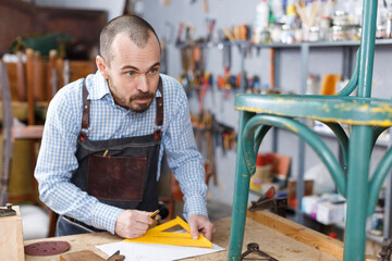 Craftsman making drawing of vintage chair on paper in woodwork studio