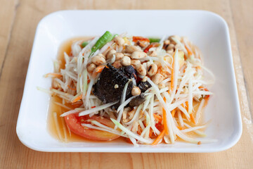 Papaya salad with preserved crab with salt or Thai people call Som Tam Poo in white plate on wooden table is a famous food.