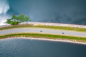 aerial view of road with cars crossing over deep blue lake in summer day