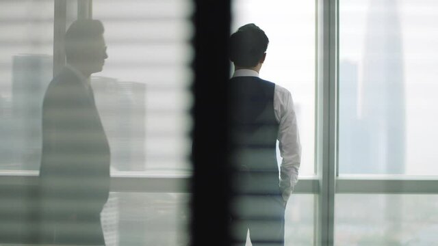 mature asian manager comforting young business man standing in front of window