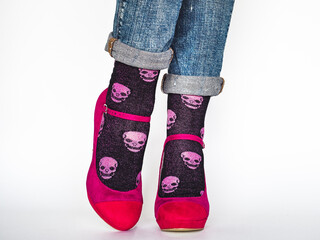 Women's legs, trendy shoes, blue jeans and variegated, long socks on a white, isolated background. Close-up. Concept of style and elegance