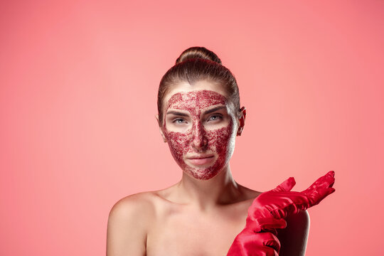 Natural cosmetic. Portrait of a charming brunette with a strawberry scrub or mask on her face in red gloves. Pink studio background. Organic