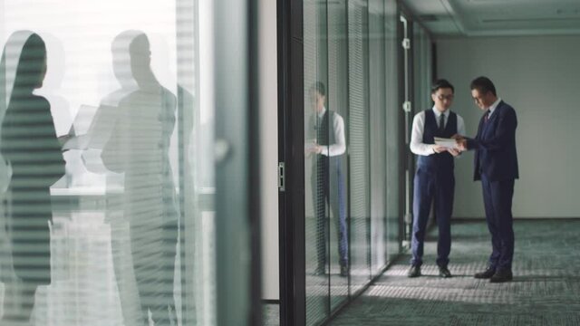 two asian corporate executives standing in hallway discussing business in modern office